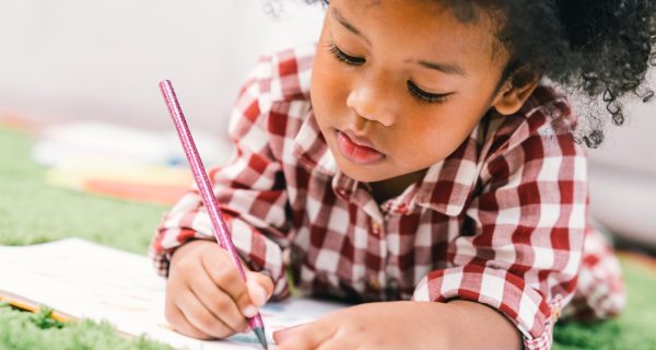 Cute young African American kid girl drawing or painting with colored pencil. Kindergarten children education, or preschool child study at home concept